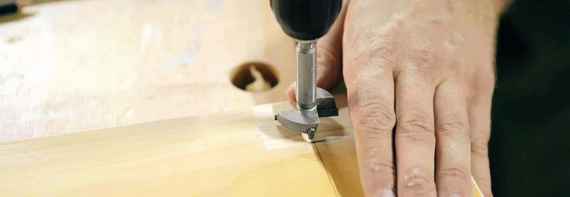 Hand führt Bohrmaschine ins Holz