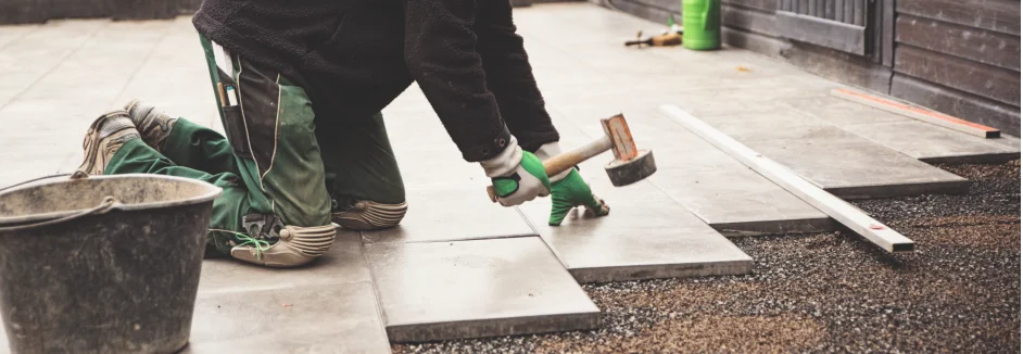 Person verlegt Terrassenplatten mit einem Gummihammer
