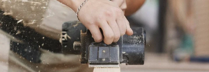 Person hobelt Holz mit elektrischem Hobel