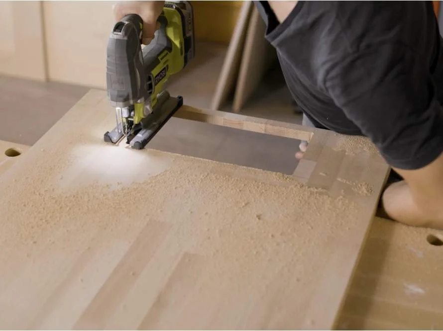 Person sägt Holzplatte mit Stichsäge