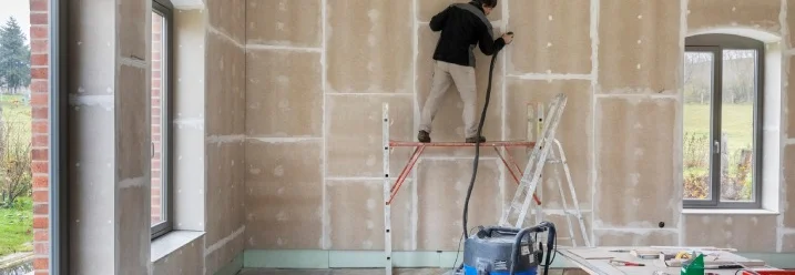 Eine Person schleift eine Trockenbauwand mit einer Schleifmaschine.