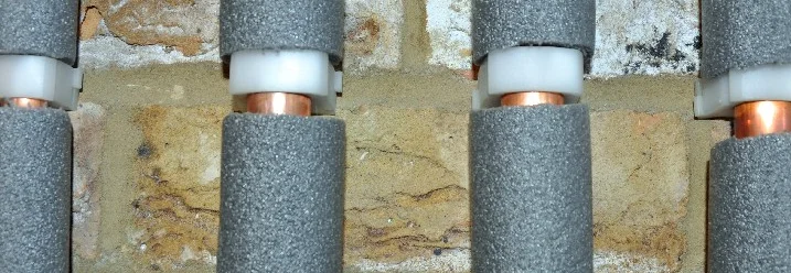 Isolierte Heizungsrohre an Ziegelwand.