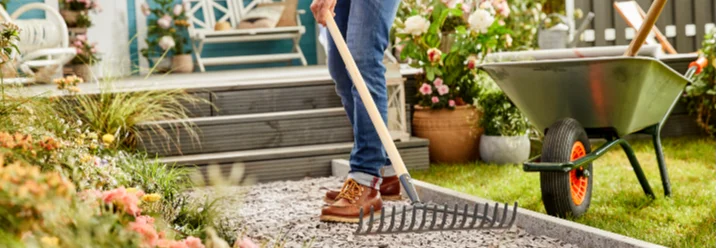 Person harkt Kiesweg im Garten
