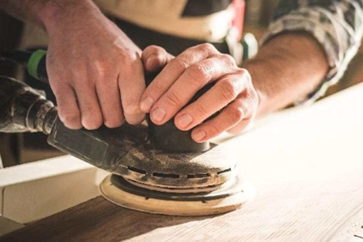 Person schleift Holz mit Schleifmaschine