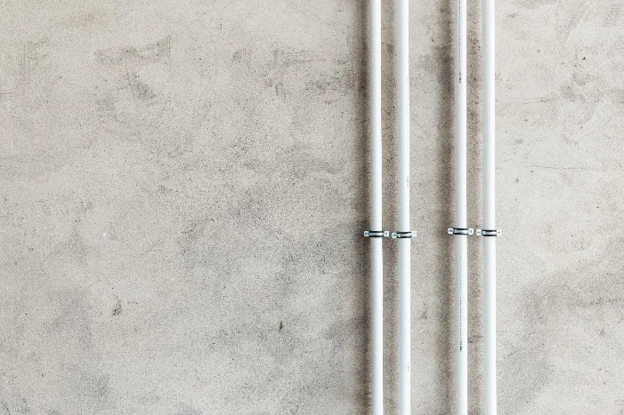 Vier weiße Rohre an Betonwand