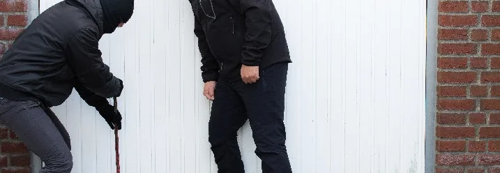 Zwei Personen in schwarz gekleidet, versuchen mit einem Brecheisen eine Tür aufzubrechen.