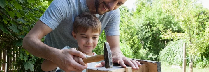 Person und Kind bauen mit Hammer einen Nistkasten