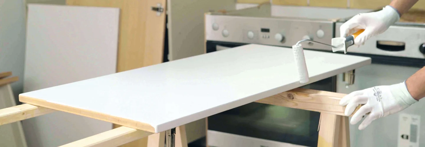 Person streicht Holzplatte mit Farbrolle weiß