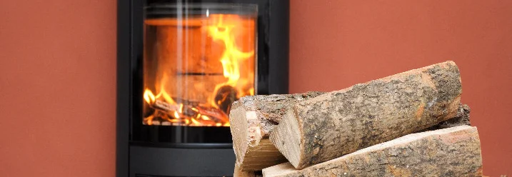 Ein Kamin mit Feuer und einem Korb mit Holzscheiten davor.