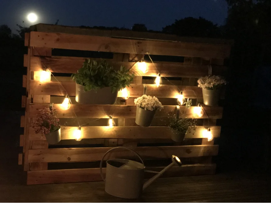 Holzwand mit Beleuchtung und Blumentöpfen