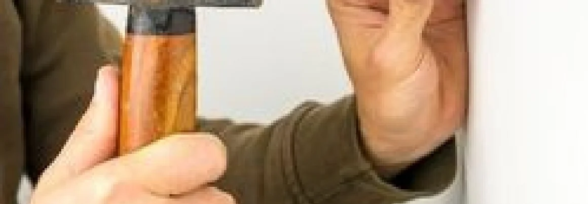 Hand schlägt Dübel mit Hammer in Wand