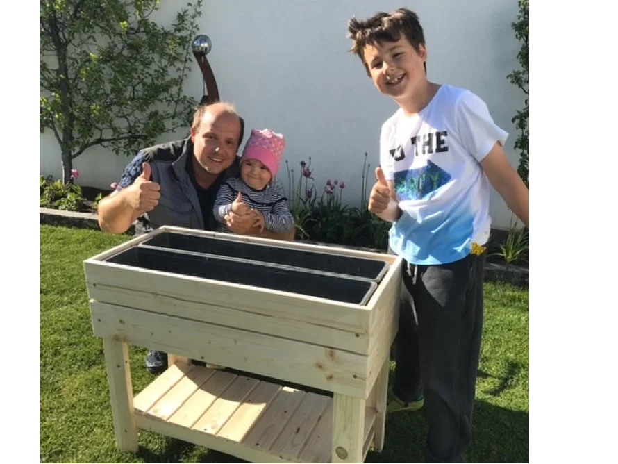Drei Personen stehen hinter einem Hochbeet aus Holz.