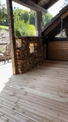 Eine überdachte Holzterrasse mit einem Stapel Brennholz und Blick ins Grüne.