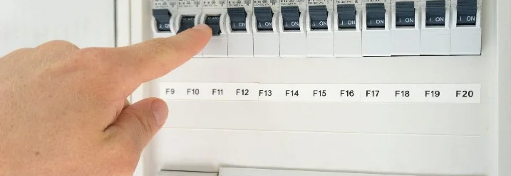 Eine Hand schaltet einen Sicherungsautomat in einem Sicherungskasten ein.
