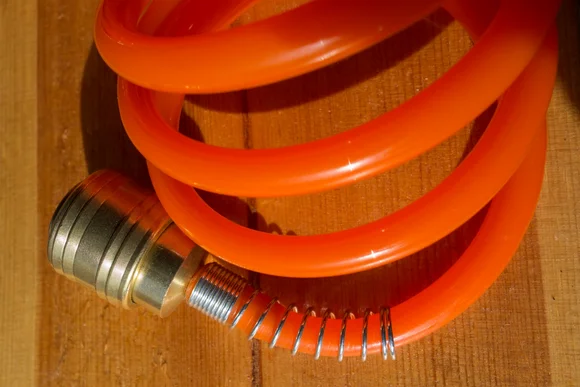 Aufgerollter orangefarbener Schlauch mit Messinganschluss