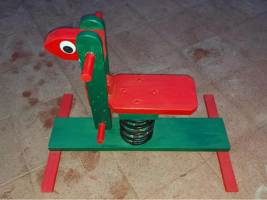 Ein grünes und rotes Spielzeugpferd mit Federn.