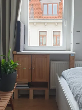Ein kleiner Holzschrank unter einem Fenster in einem Schlafzimmer.
