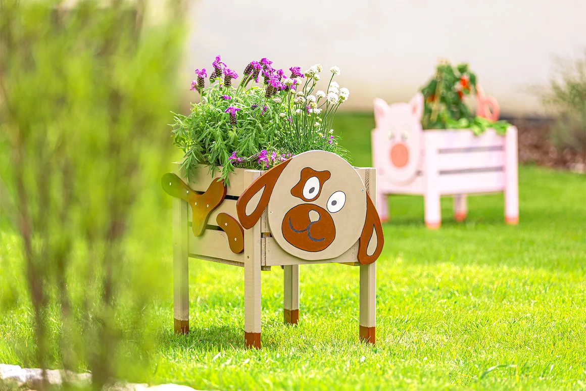 Ein bepflanzter Blumenkasten in Form eines Hundes steht auf einem Rasen.