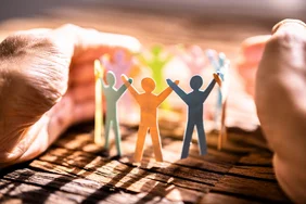 Hände schützen bunte Papierfiguren im Kreis