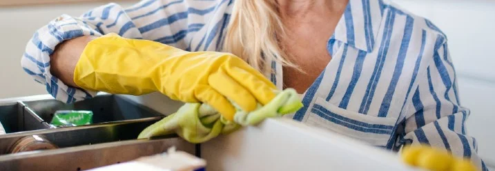 Person reinigt Küchenschrank mit Lappen.