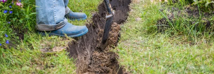 Person gräbt mit Spaten einen Graben in der Erde.