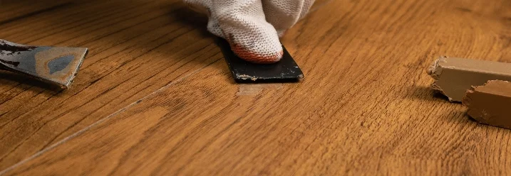 Hand mit Spachtel und Reparaturwachs auf Laminat