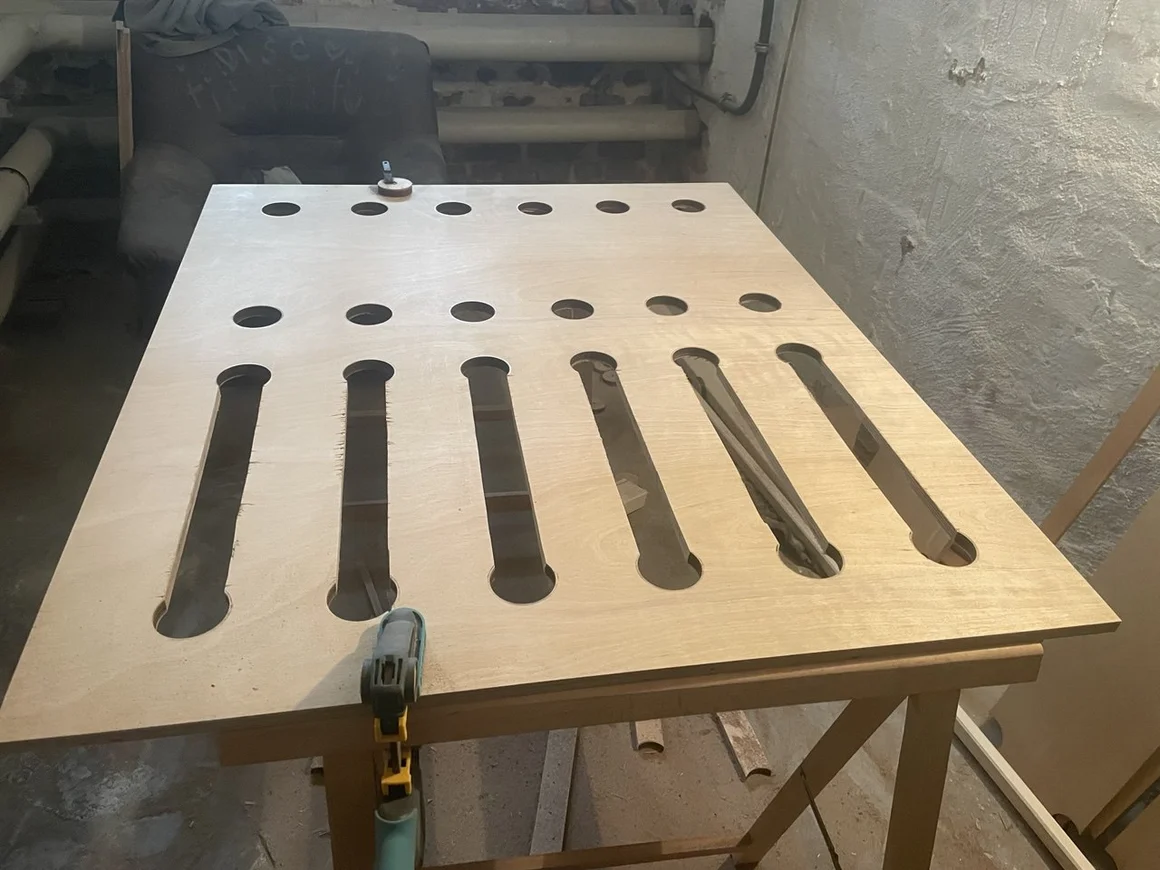 Eine Holzplatte mit runden und länglichen Ausschnitten, fixiert mit einer Schraubzwinge.