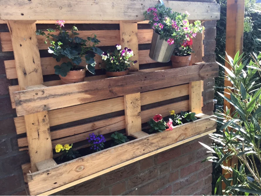 Blumenkasten aus Palettenholz an einer Backsteinmauer
