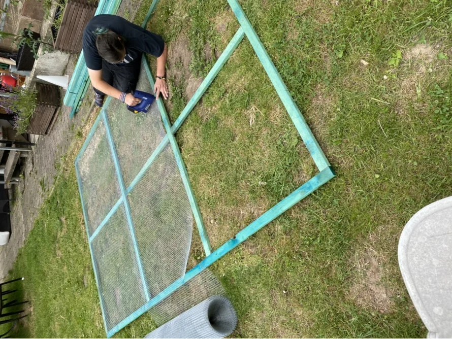 Person baut mit einem Tacker einen Holzrahmen mit Draht zusammen.