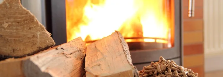 Holzscheite und Holzpellets vor brennendem Kaminofen