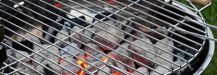 Nahaufnahme eines Holzkohlegrills mit glühender Kohle und aufgelegtem Grillrost.