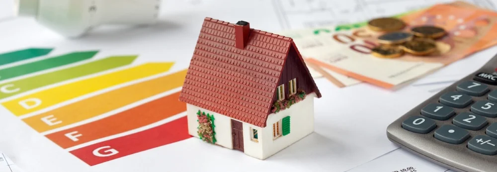 Hausmodell auf einem Energieausweis, daneben Geld und ein Taschenrechner.