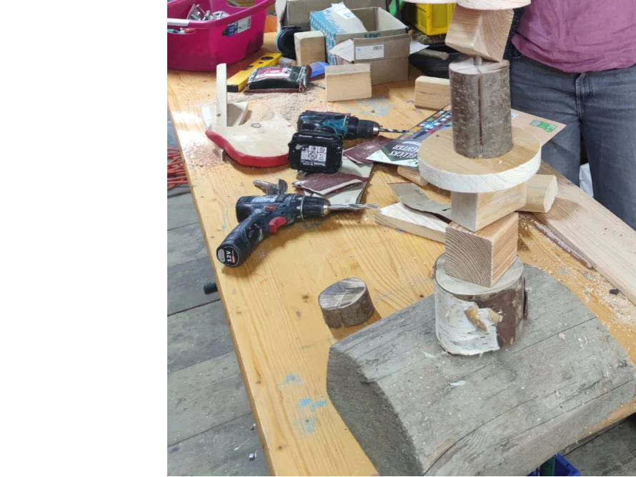 Eine unfertige Holzskulptur steht auf einer Werkbank neben zwei Akkuschraubern.