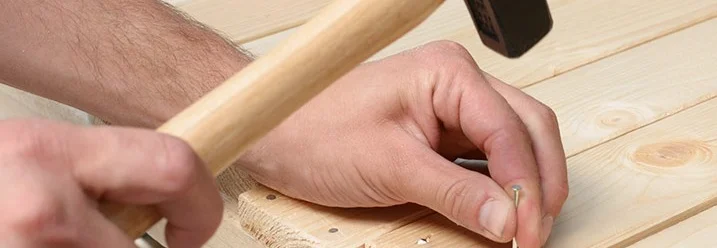 Person hämmert einen Nagel in Holz.