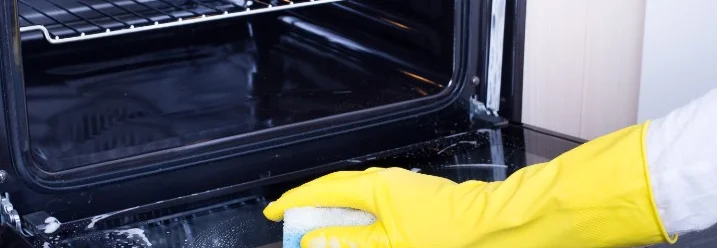 Hand in Gummihandschuh reinigt Backofen