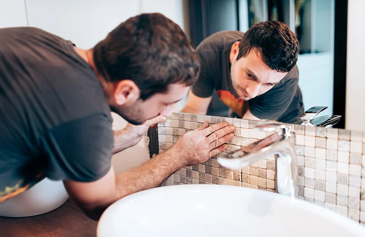 Person bringt Mosaikfliesen an Badezimmerwand an