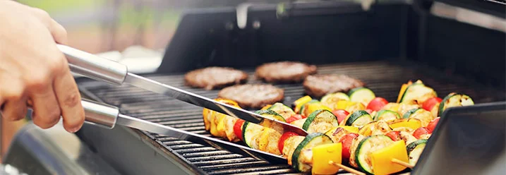 Person grillt Gemüse und Burger mit Grillzange