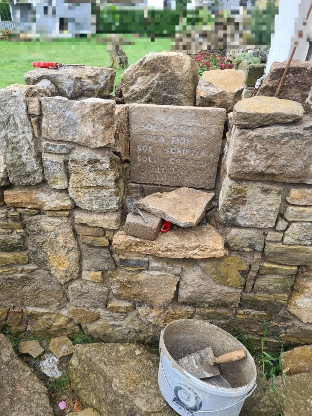 Eine im Bau befindliche Steinmauer mit einer eingravierten Gedenktafel.