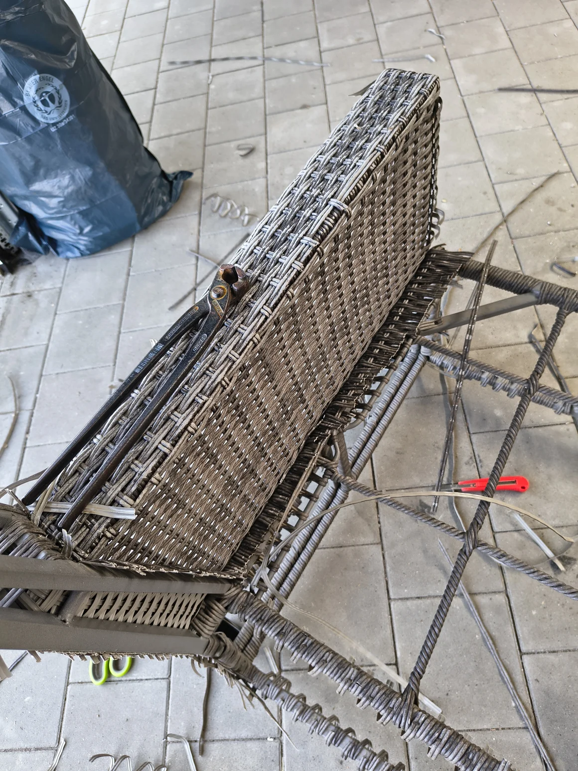 Ein kaputter Korbstuhl wird mit einem Cuttermesser und einer Zange zerlegt.