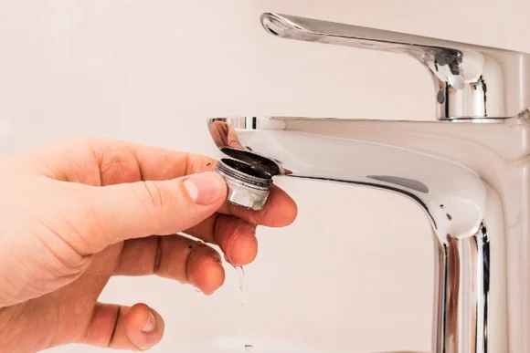 Hand nimmt verkalkten Perlator aus Wasserhahn