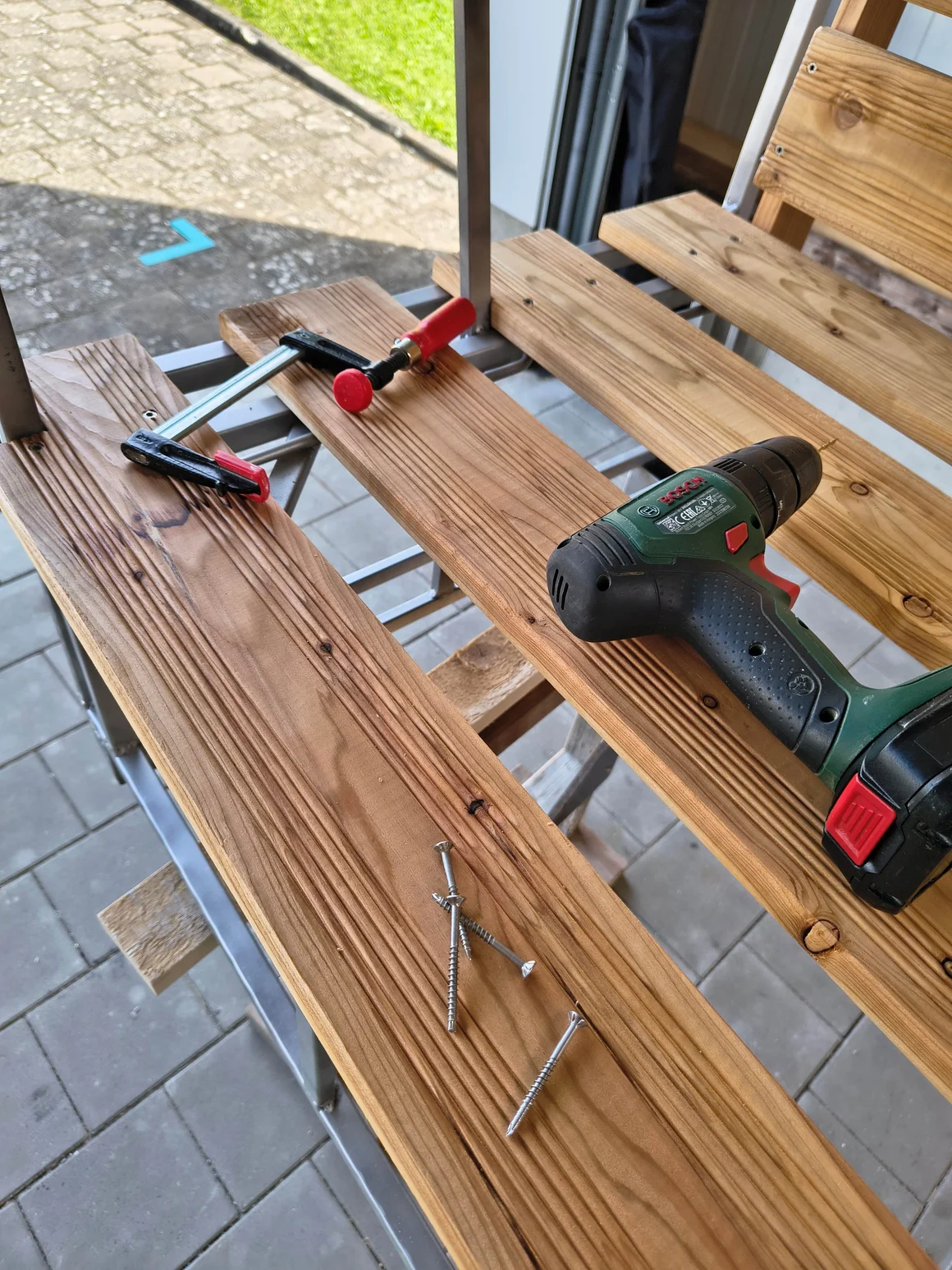 Ein Akkuschrauber, Schrauben und Zwingen bei der Montage von Holzbrettern.