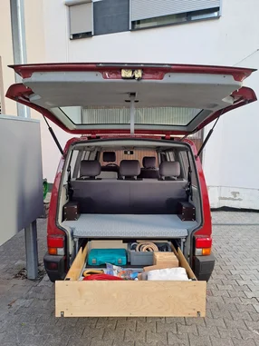 Campingausbau in einem roten Bus mit großer Schublade.