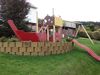 Ein Spielplatz im Garten mit einem Spielgerüst in Form eines Schiffes und einer Rutsche