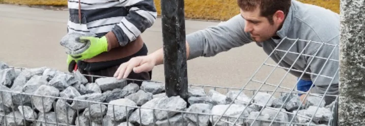 Zwei Personen bauen eine Gabione auf