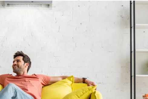 Person entspannt auf gelbem Sofa unter einer Klimaanlage.