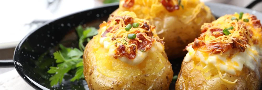 Gefüllte Ofenkartoffeln mit Käse und Speck in einer schwarzen Pfanne.