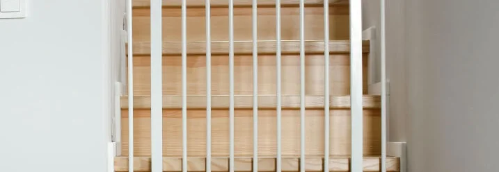 Ein weißes Treppenschutzgitter ist oben auf einer Holztreppe angebracht.
