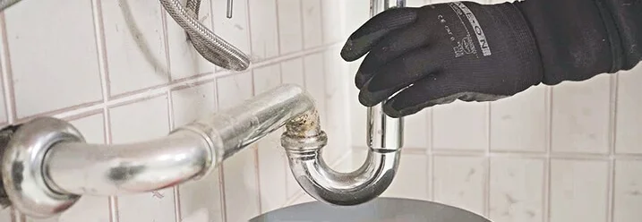 Person repariert Siphon unter Spüle.