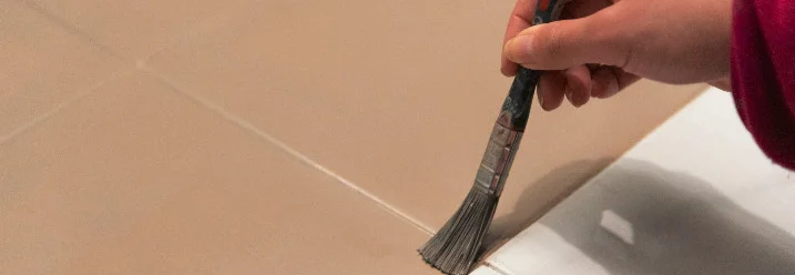Hand trägt Farbe mit einem Pinsel auf Fliesen auf