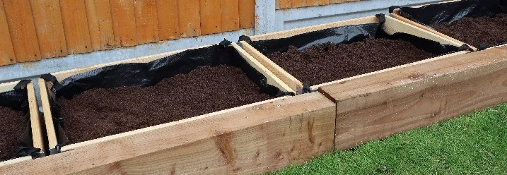Drei Hochbeete aus Holz mit Erde gefüllt